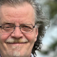 Close-up of an older man with glasses and a gray goatee smiling at the camera, outdoors.